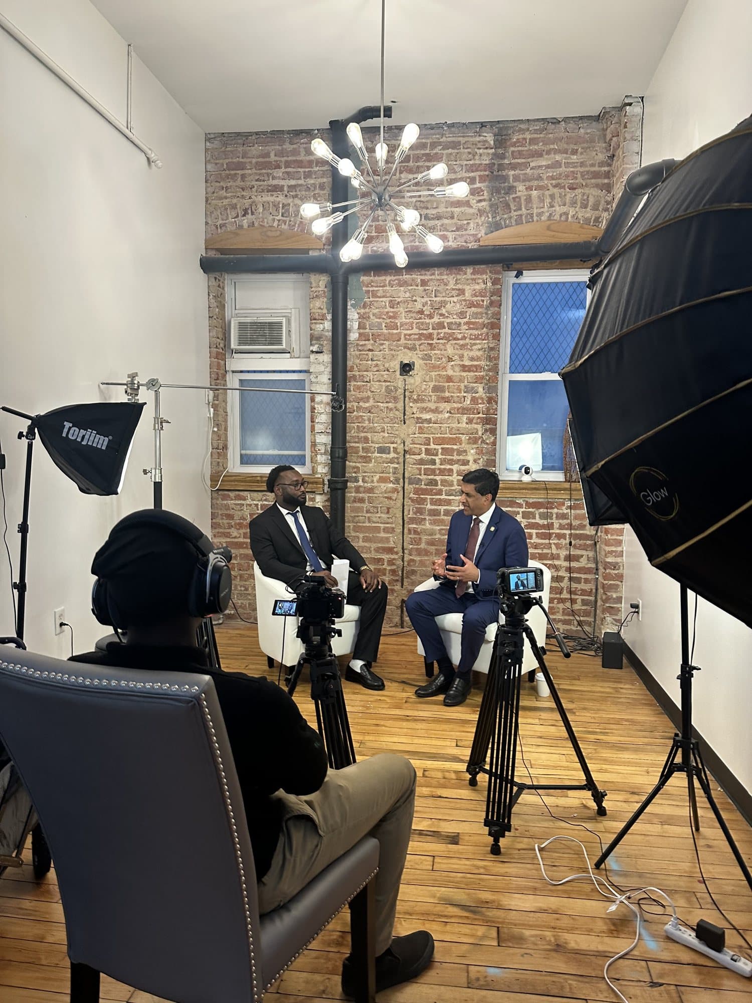 Behind the scenes of Brian Allen interviewing Rep. Ro Khanna on a brick-wall set with studio lights