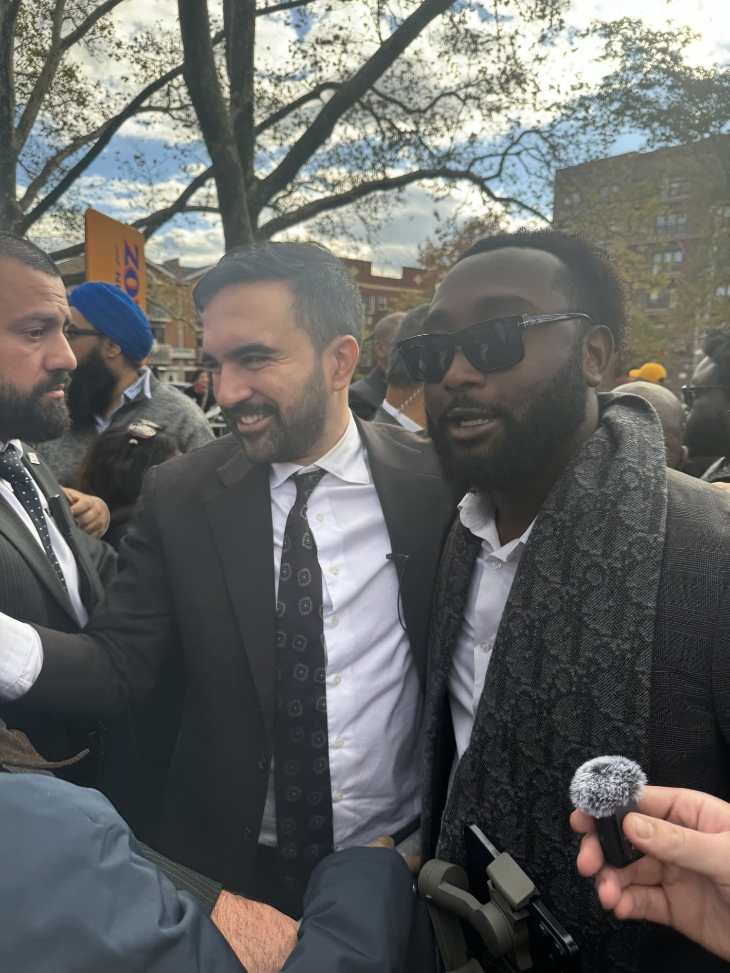 Brian Allen beside Zohran Mamdani at an outdoor press scrum